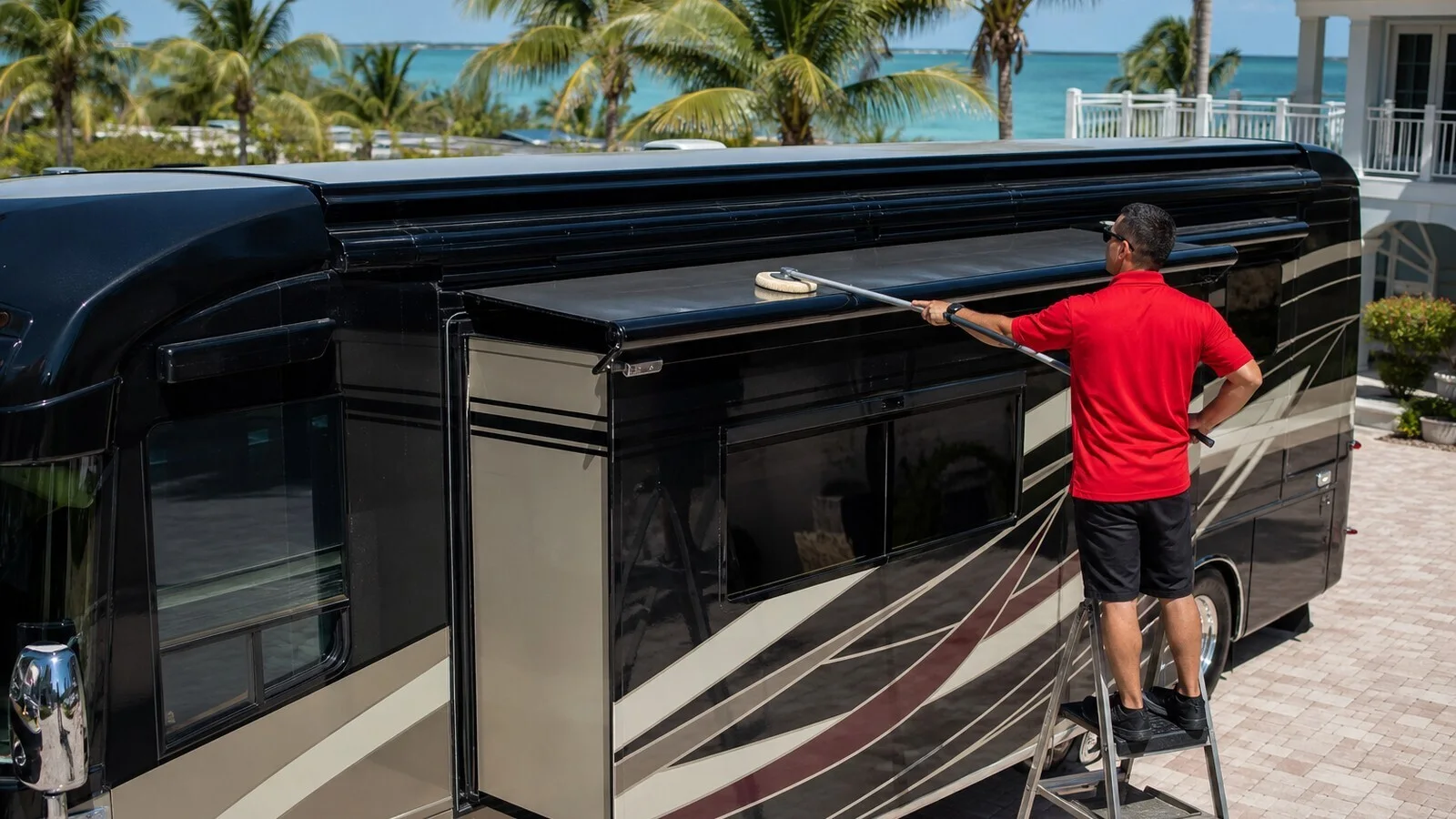 Leoserve technician in a solid red shirt using a wool wash pad on a telescoping extension pole to clean the top surface of an extended RV slide-out in the Florida Keys