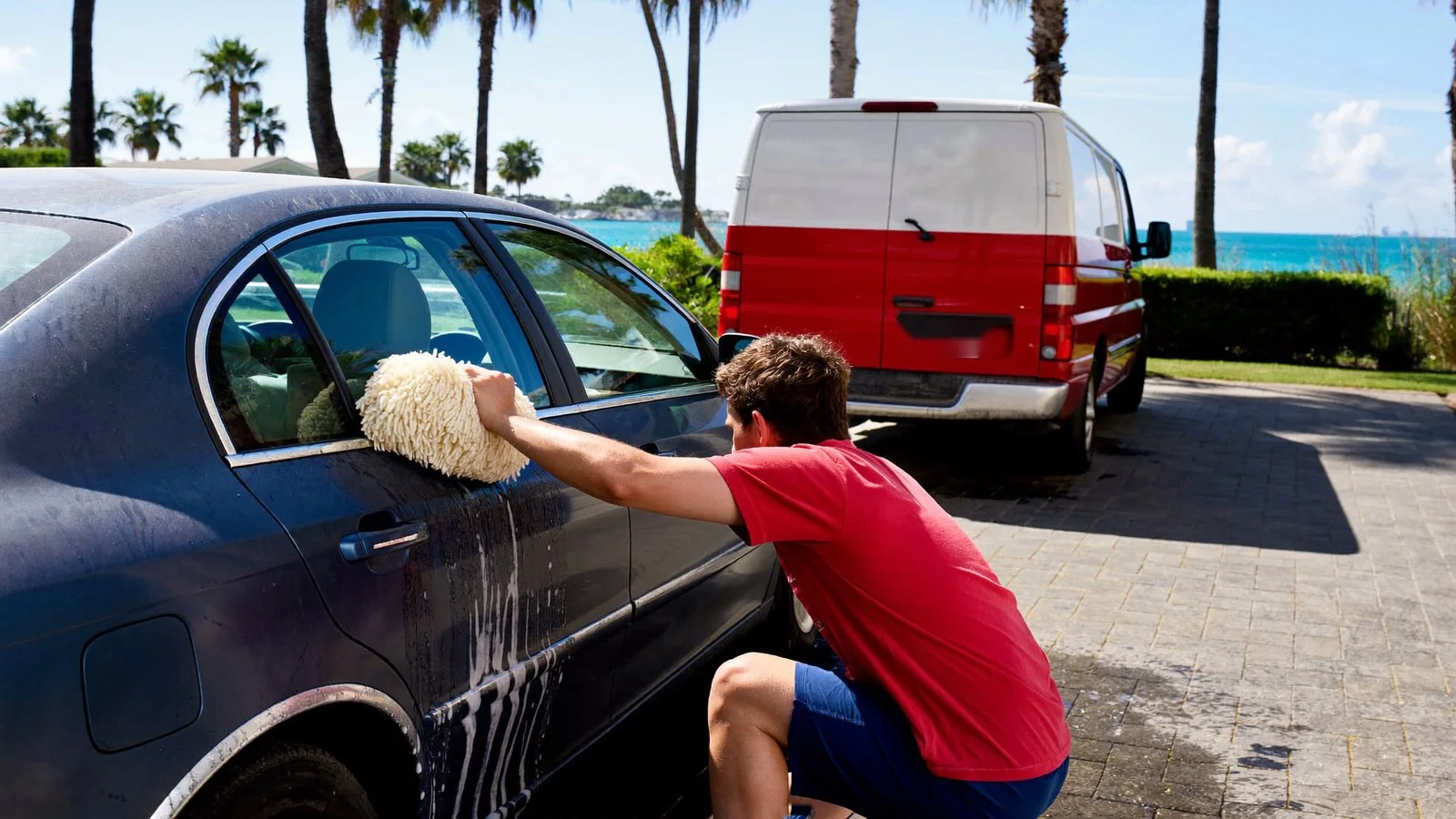 Leoserve crew member hand-washing a car's lower panel with a wool wash pad