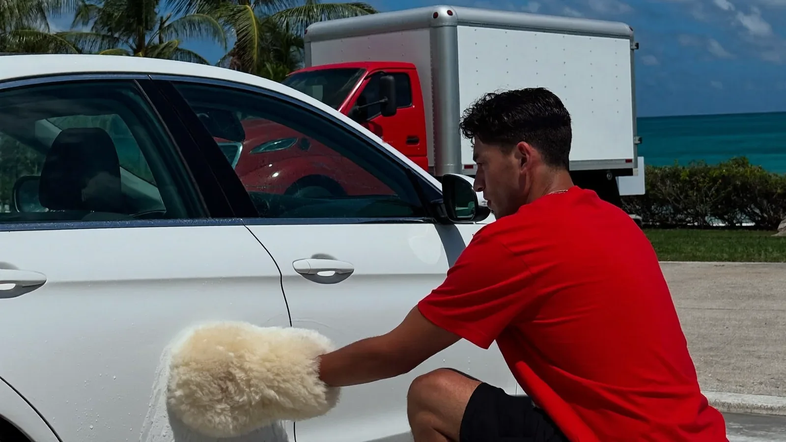 Leoserve crew member hand-washing the lower door panel of a car with a wool wash mitt
