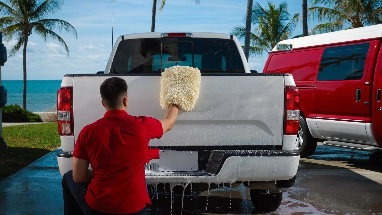 Leoserve crew member hand-washing a pickup truck tailgate with a wool wash pad